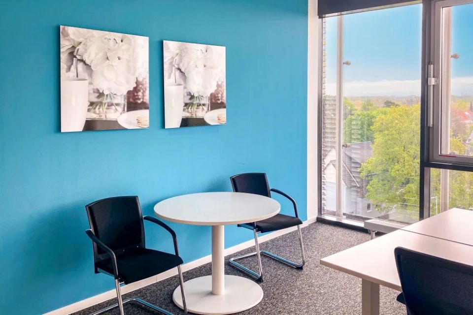 Sitzbereich mit rundem Tisch, Stühlen, blauer Wand und heller Fensterfront