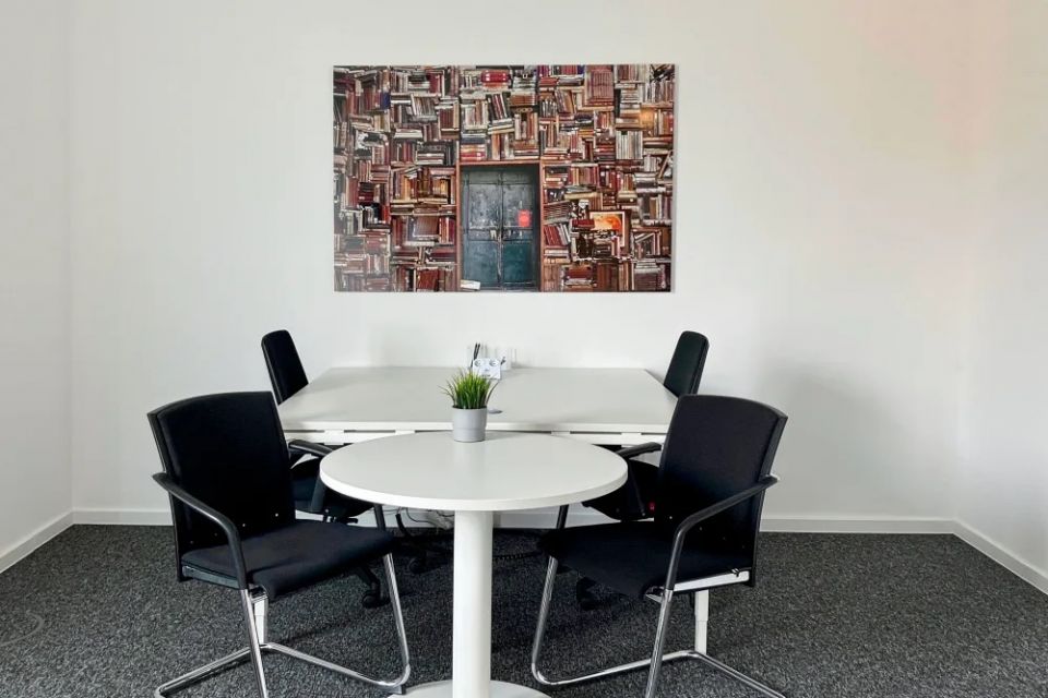 Kleiner Besprechungsbereich mit rundem Tisch, Stühlen und Wandbild